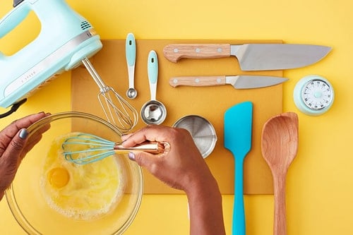 A photo of a person whisking an egg next to kitchen tools
